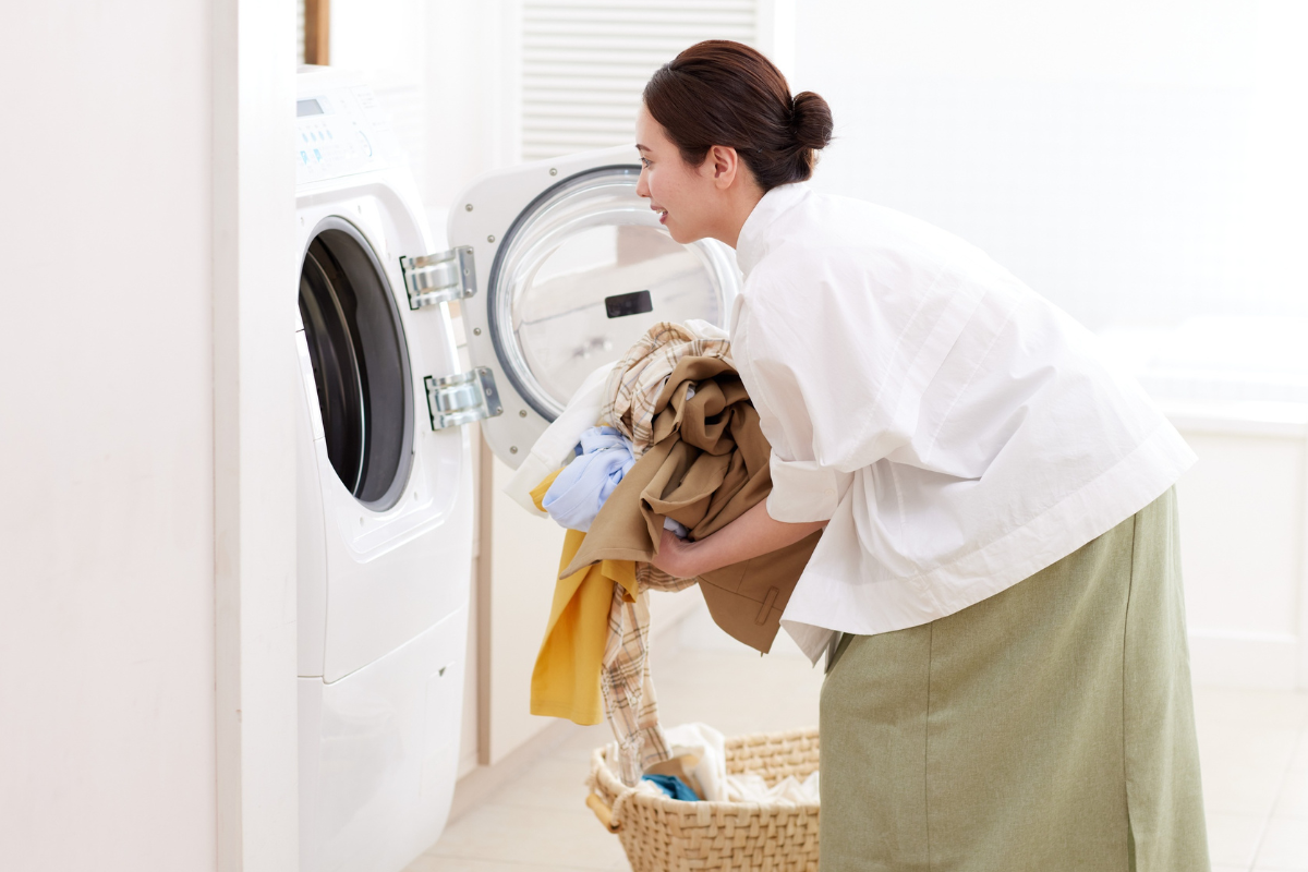 perempuan memasukkan baju ke mesin cuci